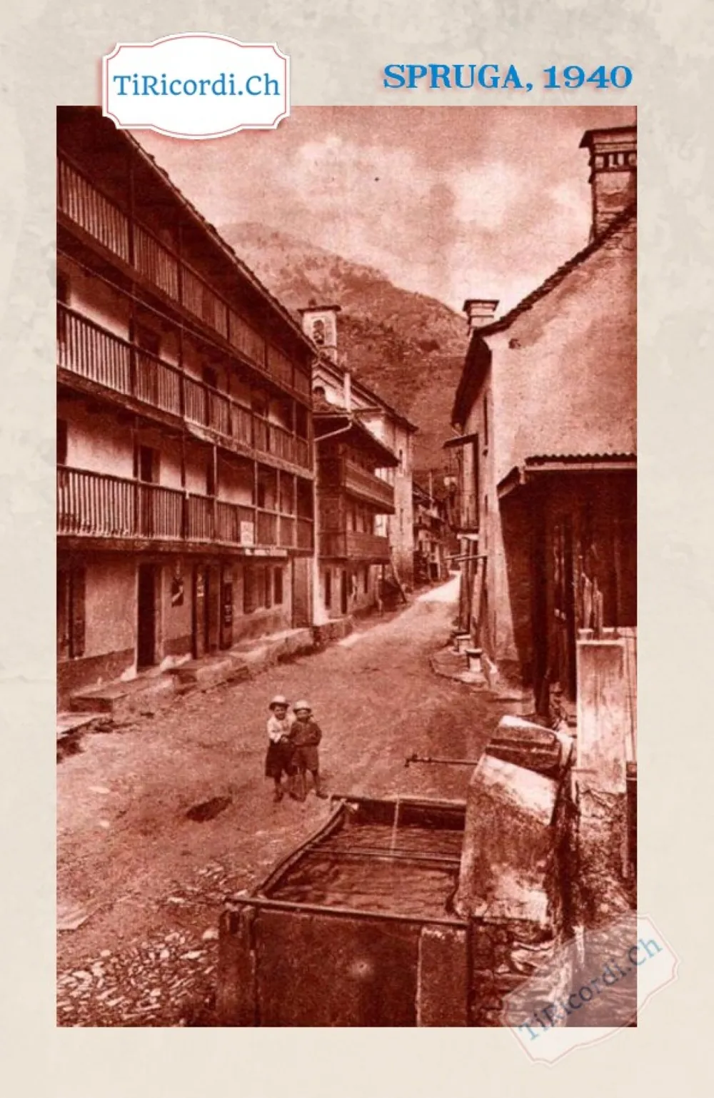 Spruga, 1940: la contrada con le lunghe logge di legno, la fontana in pietra e due bambini in mezzo alla strada